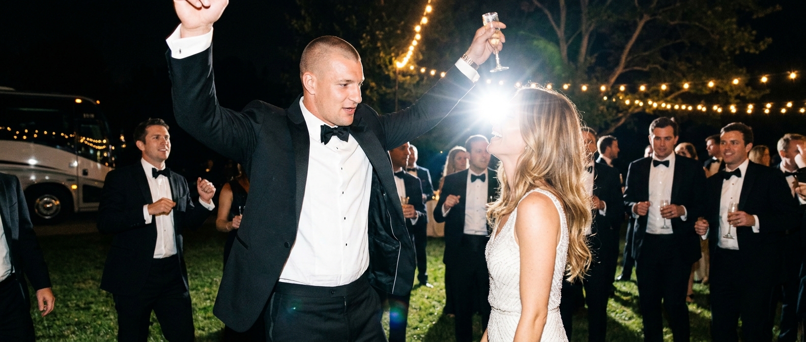 A blurry, energetic flash photograph of a couple in wedding attire laughing and dancing with guests at an outdoor night re…